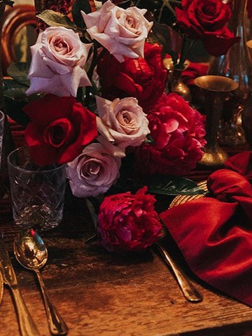 Blush and red roses with peonies on a wooden table beside a red napkin