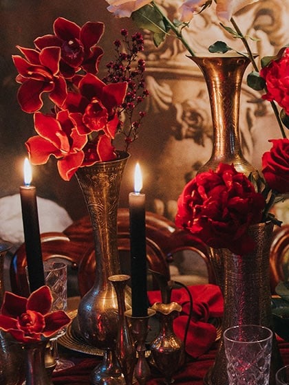 Red orchids in brass vases beside black taper candles
